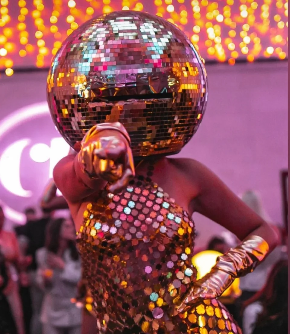 Disco ball head dancer wearing a mirrored headpiece, sequinned costume and gold gloves