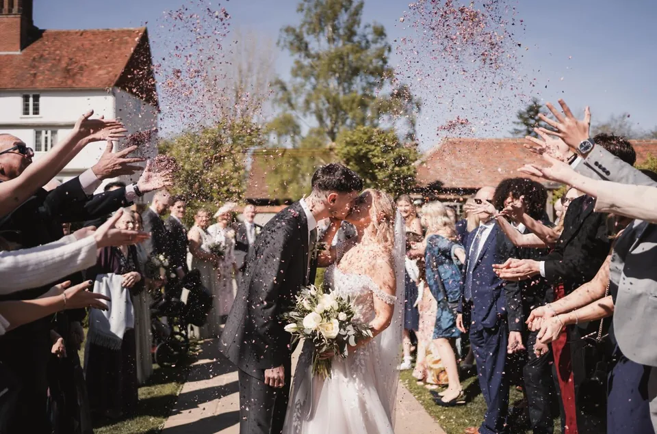 Newly married couple kissing beneath confetti at Houchins wedding venue in Essex
