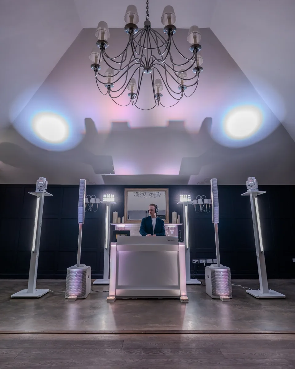 White DJ booth with line-array sound system and wedding lighting setup